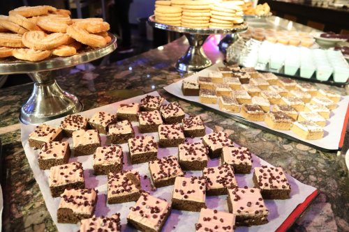 A variety of desserts displayed on trays, including cookies, layered treats, and chocolate-covered squares.