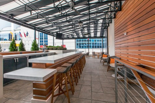 A modern rooftop bar with a sleek design, featuring a long counter, wooden accents, and comfortable seating.