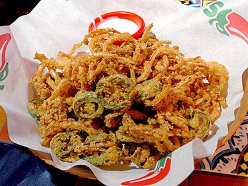 A basket of crispy fried onion rings and jalapeño slices served with a dipping sauce.