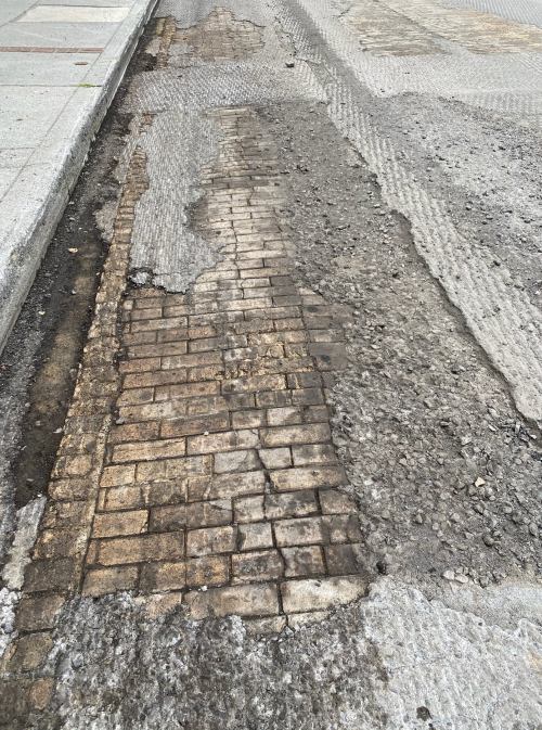 A damaged street showing cracked pavement and exposed brick beneath a layer of gravel and debris.