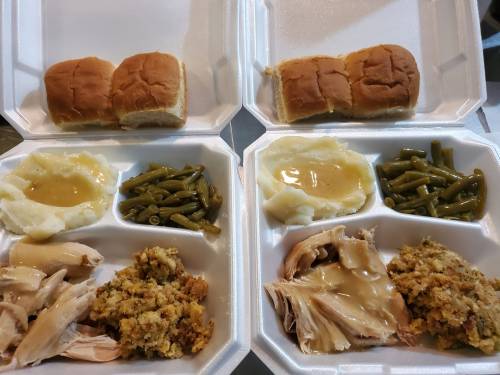 Two takeout containers with chicken, stuffing, mashed potatoes, green beans, gravy, and three dinner rolls each.