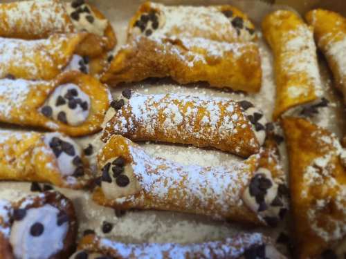 A close-up of freshly made cannoli dusted with powdered sugar and filled with chocolate chips.
