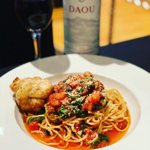 A plate of spaghetti topped with tomato sauce and herbs, accompanied by a piece of bread and a bottle of DAOU wine.