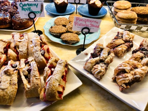 A display of assorted pastries, including cranberry rolls, raspberry ricotta strudels, and cookies on colorful plates.