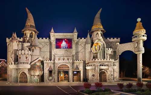 A whimsical castle-themed building with towers and turrets, illuminated at night against a dark sky.