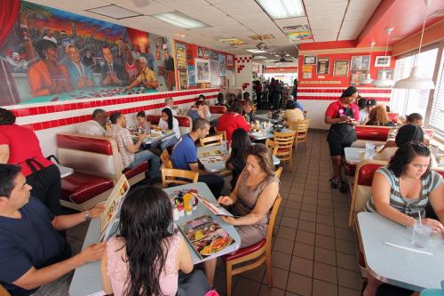 A busy diner with patrons eating and chatting, colorful murals on the walls, and a lively atmosphere.