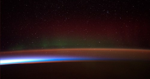 A stunning view of Earth from space, featuring a colorful aurora against a starry night sky.
