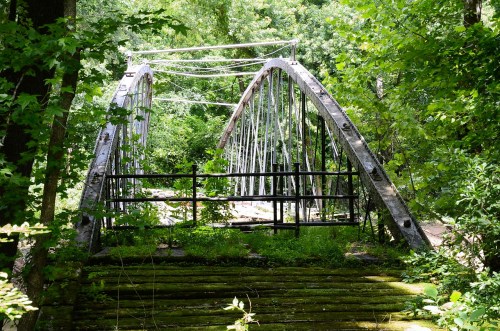 An old, abandoned arch bridge surrounded by lush green trees and overgrown vegetation.