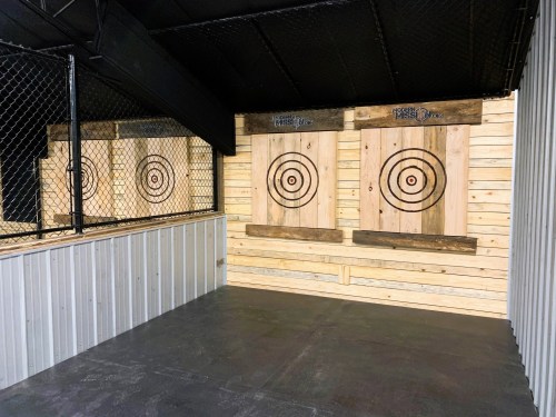 Indoor axe throwing range with wooden targets and a fenced area.