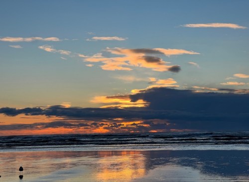 A serene beach at sunset, with colorful clouds reflecting on the water's surface.