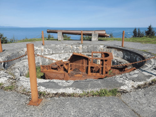 Rusty remnants of a coastal artillery gun on a scenic overlook, with ocean views in the background.