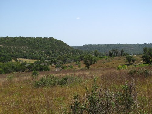A scenic view of rolling hills and green vegetation under a clear blue sky.