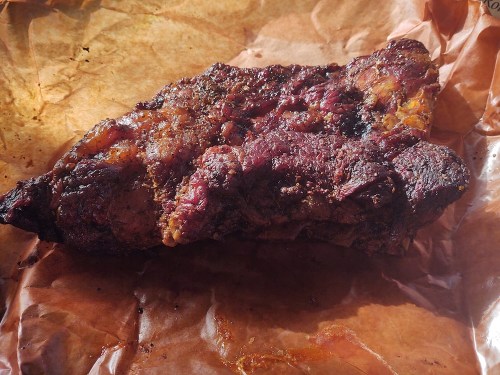 A piece of smoked meat resting on brown parchment paper, showcasing a crispy, charred exterior.