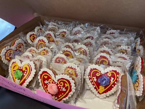 A box filled with decorated heart-shaped cookies, each individually wrapped and adorned with colorful icing.