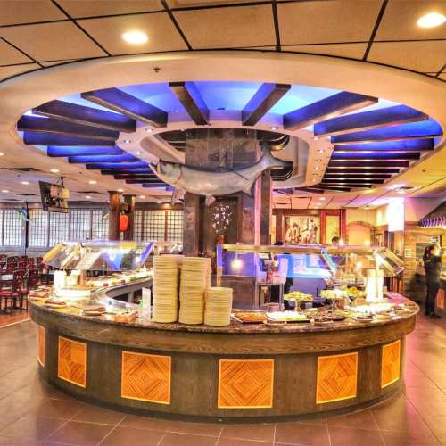 A circular buffet station with various dishes, surrounded by seating and colorful lighting in a restaurant.