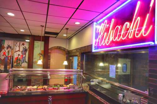 A vibrant restaurant interior featuring a buffet with a neon "Hibachi" sign and colorful wall art.
