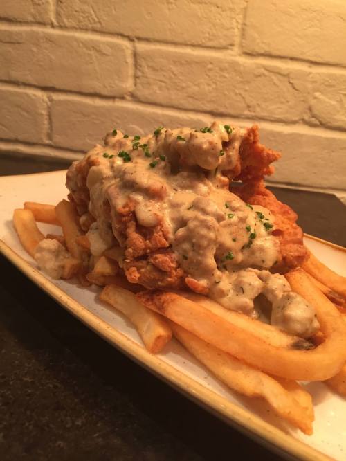 A plate of crispy fried chicken topped with creamy gravy, served over a bed of golden French fries.