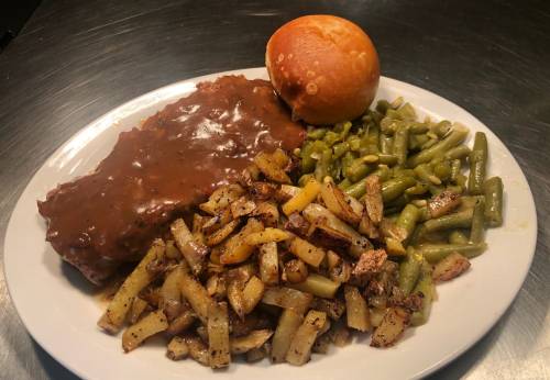 A plate of food featuring meat with gravy, green beans, seasoned potatoes, and a roll.