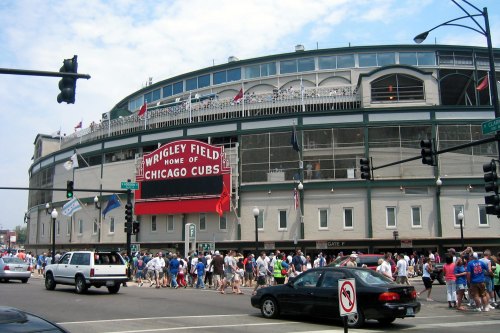 Crowd of fans walking past Wrigley Field, home of the Chicago Cubs, with a large sign visible.