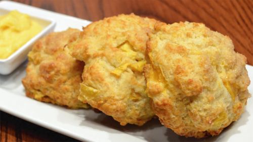 Three golden, fluffy biscuits on a white plate, accompanied by a small dish of yellow spread.