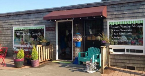 A cozy candy shop with a welcoming entrance, featuring colorful signs and outdoor seating.