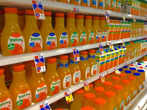 A grocery store shelf filled with various brands of orange juice in bottles and cartons.
