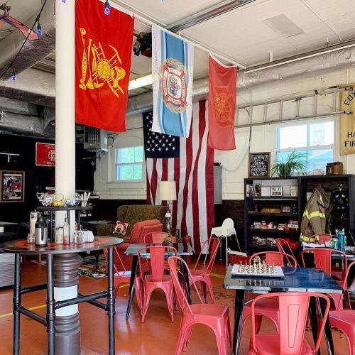 A cozy room with red chairs, a chessboard, and flags, including an American flag, in a firehouse-themed setting.
