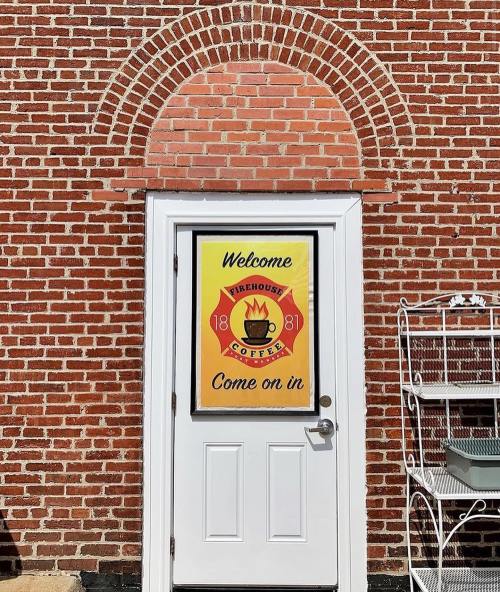 A brick wall features a welcoming door with a colorful sign for Firehouse Coffee, inviting visitors to enter.