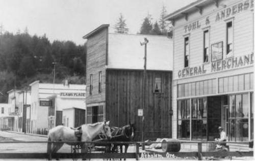 Historic black-and-white photo of a small town street with a horse-drawn carriage and general store.