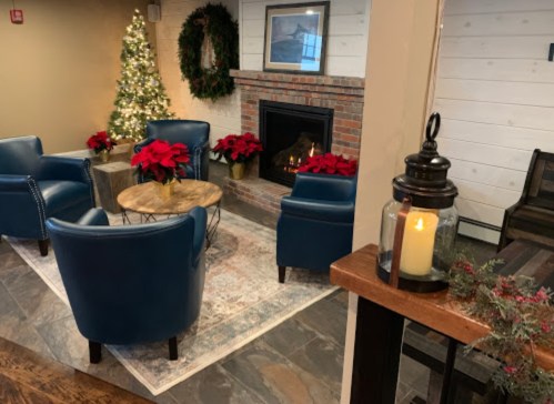 Cozy lounge area with blue chairs, a festive tree, poinsettias, and a fireplace, creating a warm holiday atmosphere.