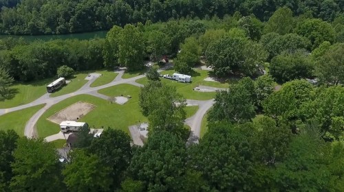 Aerial view of a green campground with winding paths, RVs, and trees near a river.