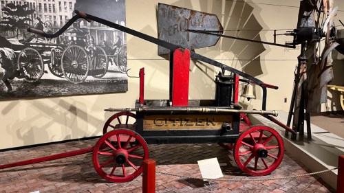 A vintage fire engine with red wheels and a black and yellow body displayed in a museum setting.