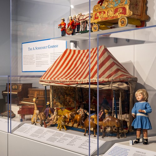 Display of vintage toys, including a circus tent, wooden animals, and a doll, showcasing the A. Schoenhut Company.