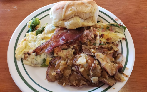 A plate of breakfast featuring scrambled eggs with vegetables, bacon, and roasted potatoes, alongside a biscuit.