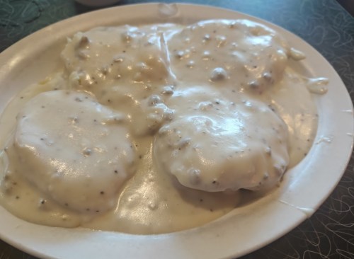 A plate of biscuits smothered in creamy sausage gravy, served on a white dish.
