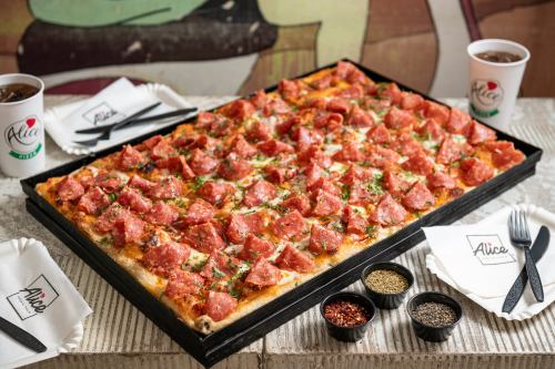 A large pepperoni pizza topped with herbs, served with drinks and condiments on a table.