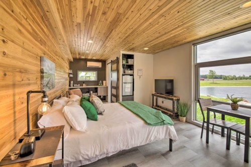 Cozy bedroom with wooden ceiling, large window, and modern furnishings, overlooking a serene outdoor view.