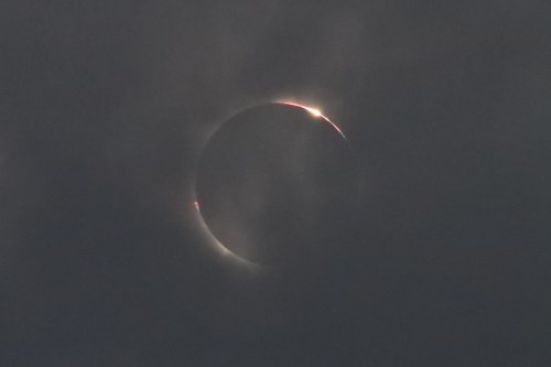 A partially obscured solar eclipse with a glowing ring visible through clouds.