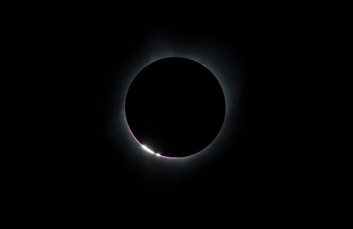 A solar eclipse with a darkened sun surrounded by a glowing corona against a black sky.