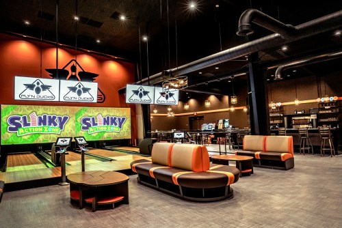 A modern entertainment venue featuring bowling lanes, seating areas, and large screens displaying vibrant graphics.