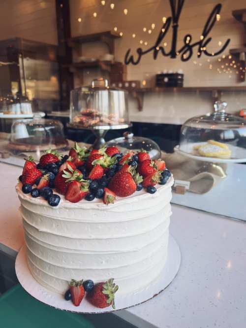 A beautifully decorated white cake topped with fresh strawberries and blueberries, displayed in a bakery.