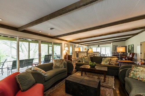 Cozy living room with plush sofas, wooden beams, and large windows overlooking a natural view.