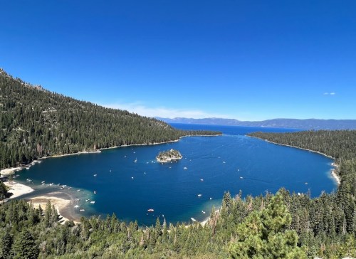 A scenic view of a blue lake surrounded by green forests and mountains, with small boats on the water.