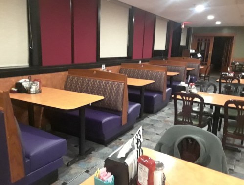Interior of a diner featuring purple booths, wooden tables, and a tiled floor, with condiments on the tables.
