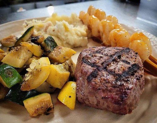 A plate featuring grilled steak, shrimp skewers, and a side of mashed potatoes with mixed grilled vegetables.