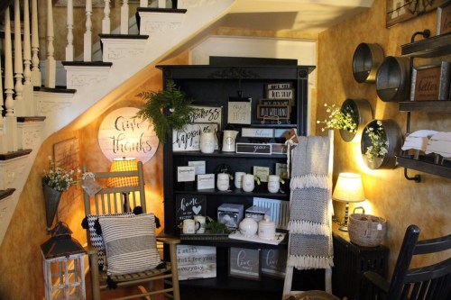Cozy interior with a black shelf displaying decorative signs, a rocking chair, and warm lighting under a staircase.