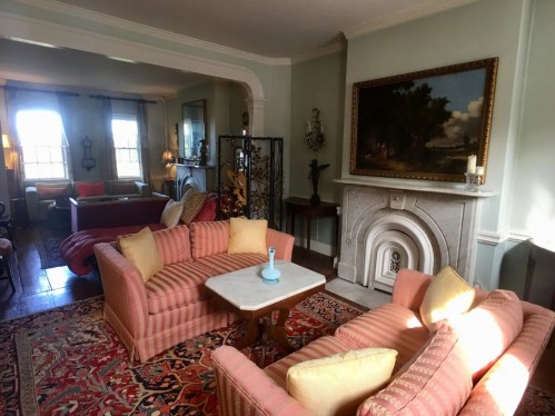 Cozy living room with pink striped sofas, a marble fireplace, and a colorful rug, featuring warm lighting and artwork.