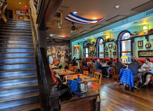 A cozy restaurant interior with wooden stairs, colorful decor, and diners enjoying meals at tables.
