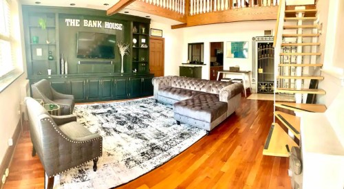 Spacious living room with a dark green accent wall, plush seating, wooden floors, and a staircase leading to an upper level.