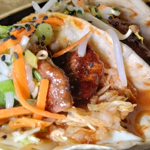 Close-up of tacos filled with grilled meat, fresh vegetables, and garnished with sesame seeds.